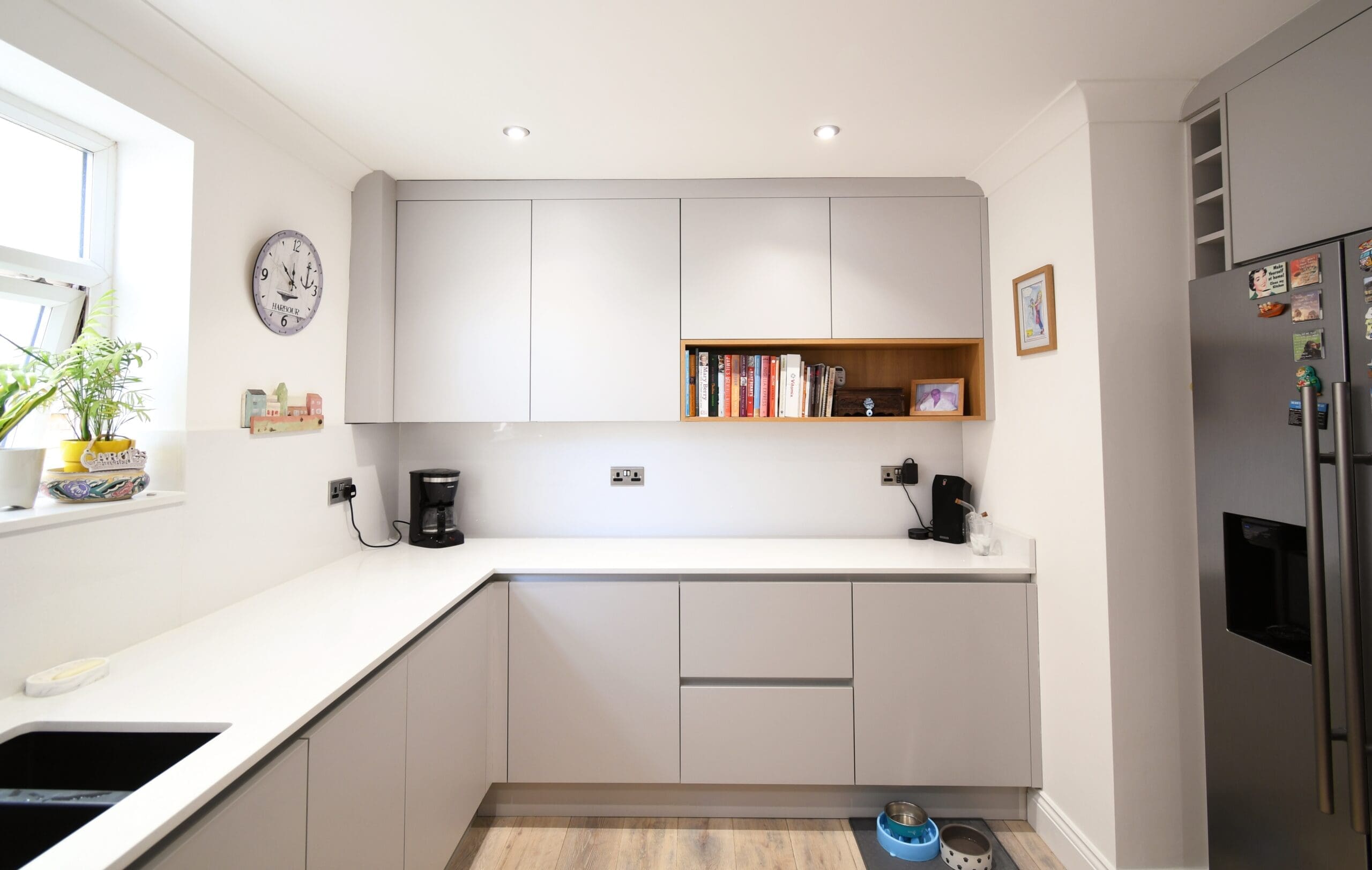 Light grey kitchen with oak open shelving area with recipe books